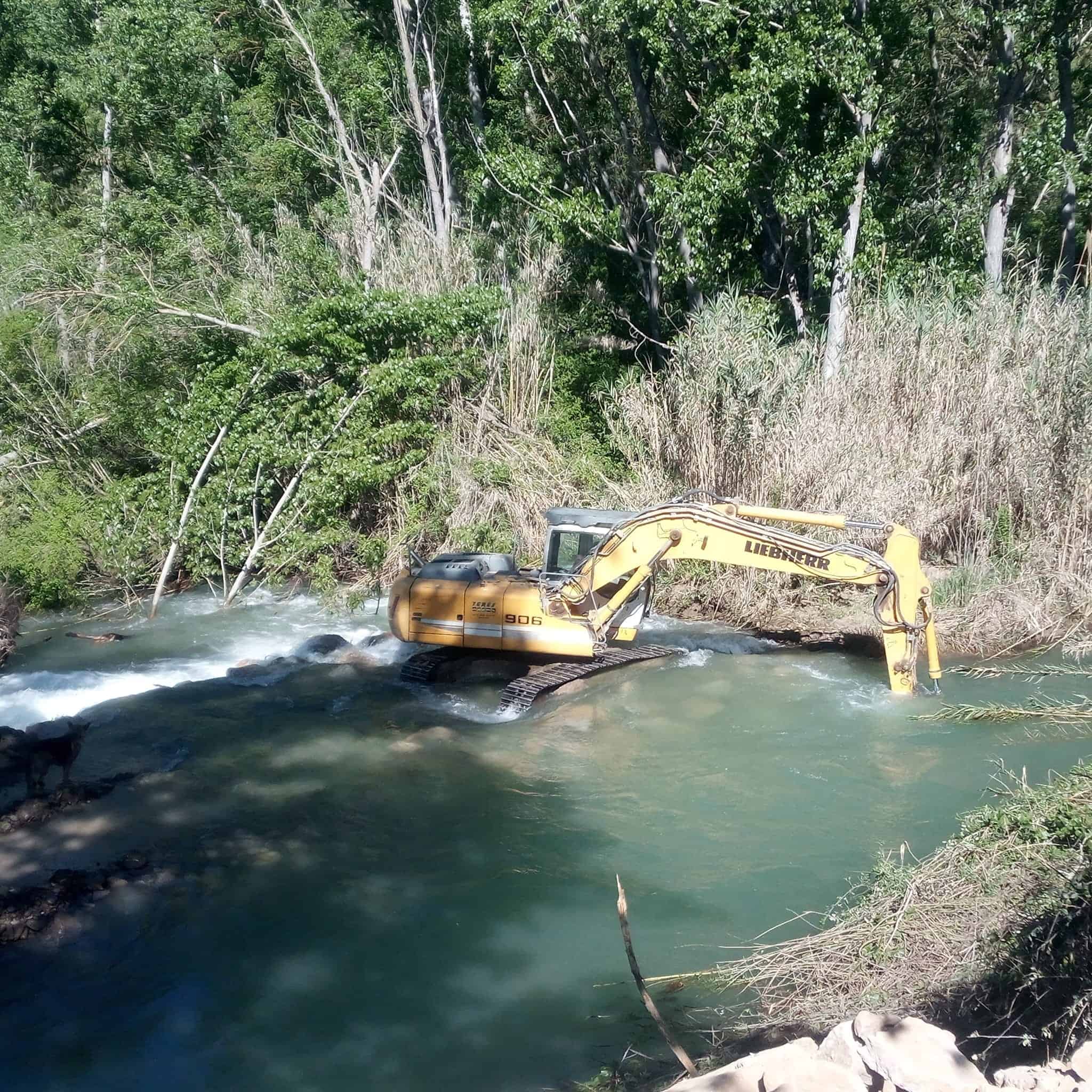 Maquinaria de excavación en río para trabajos de limpieza y mantenimiento de cauces. Servicios especializados en obras hidráulicas y conservación del medio ambiente natural. Trabajos en terrenos acuáticos con maquinaria pesada.