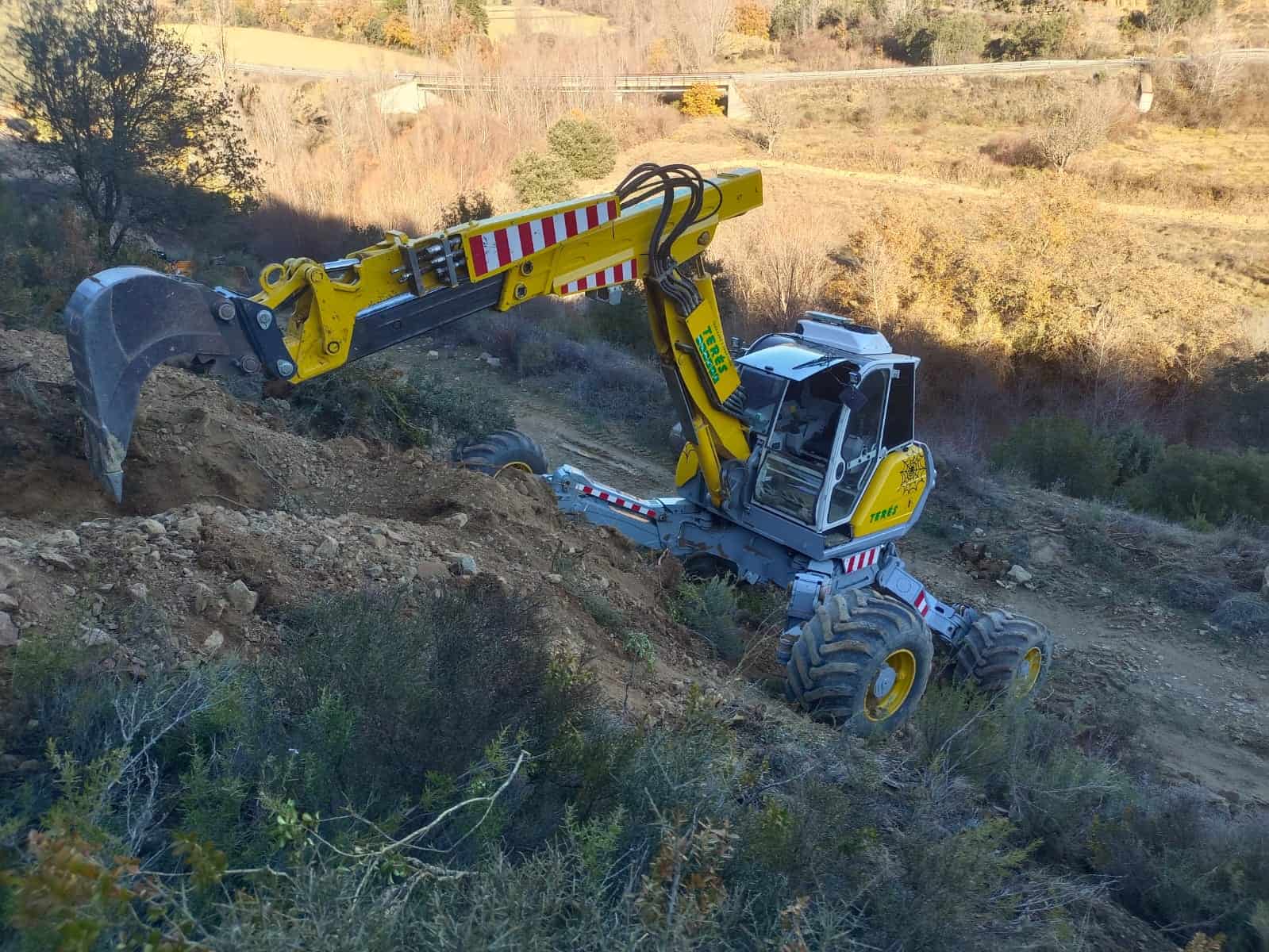 Excavadora trabajando en obras de mantenimiento y construcción en terrenos rurales, especializada en movimientos de tierra y excavaciones.