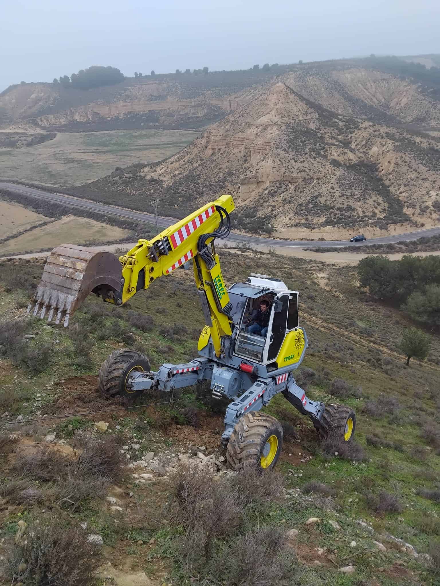 Maquinaria de obra en terrenos rurales y montaña, excavadora de ruedas en trabajos de construcción y mantenimiento de caminos rurales.