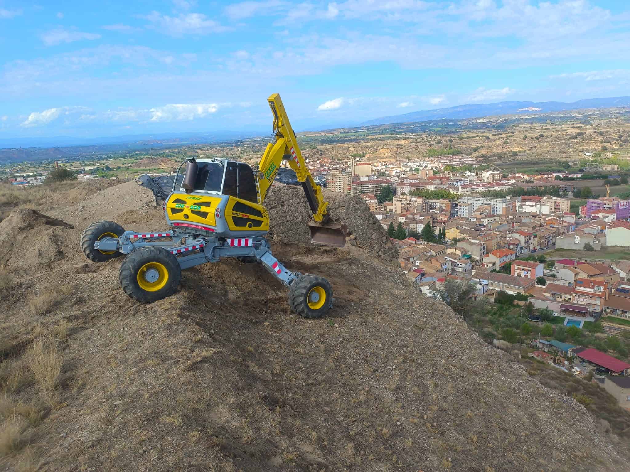 Maquinaria de excavación trabajando en obra en altura con vista panorámica de la ciudad y el campo en el fondo.