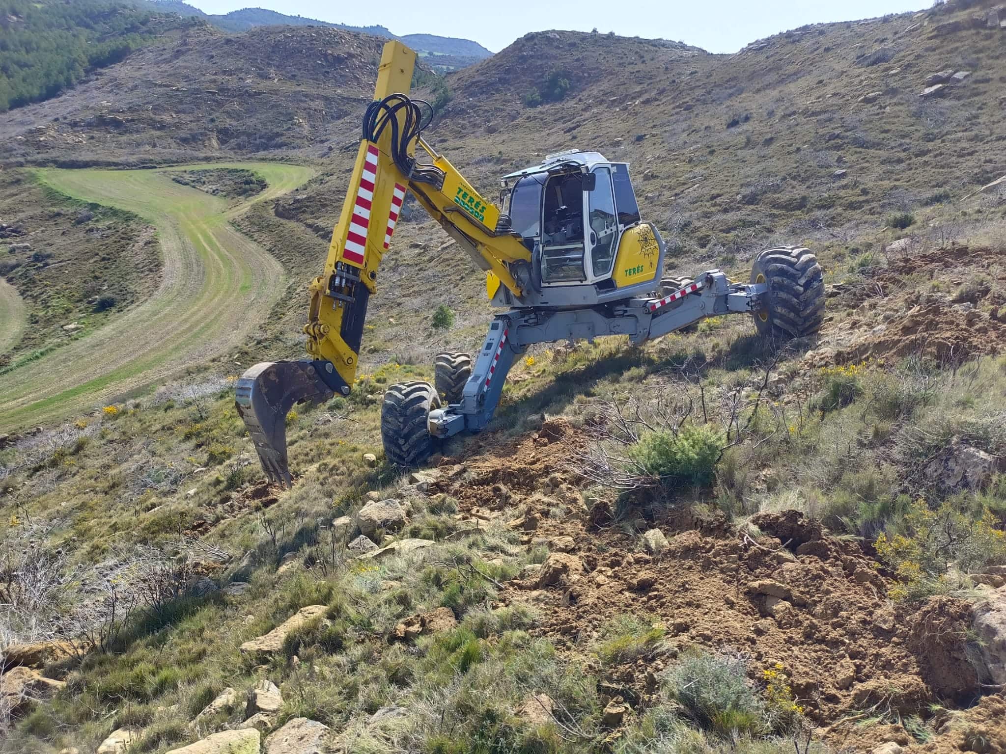 Excavadora trabajando en tarea de construcción y mantenimiento de caminos rurales y zonas de montaña.