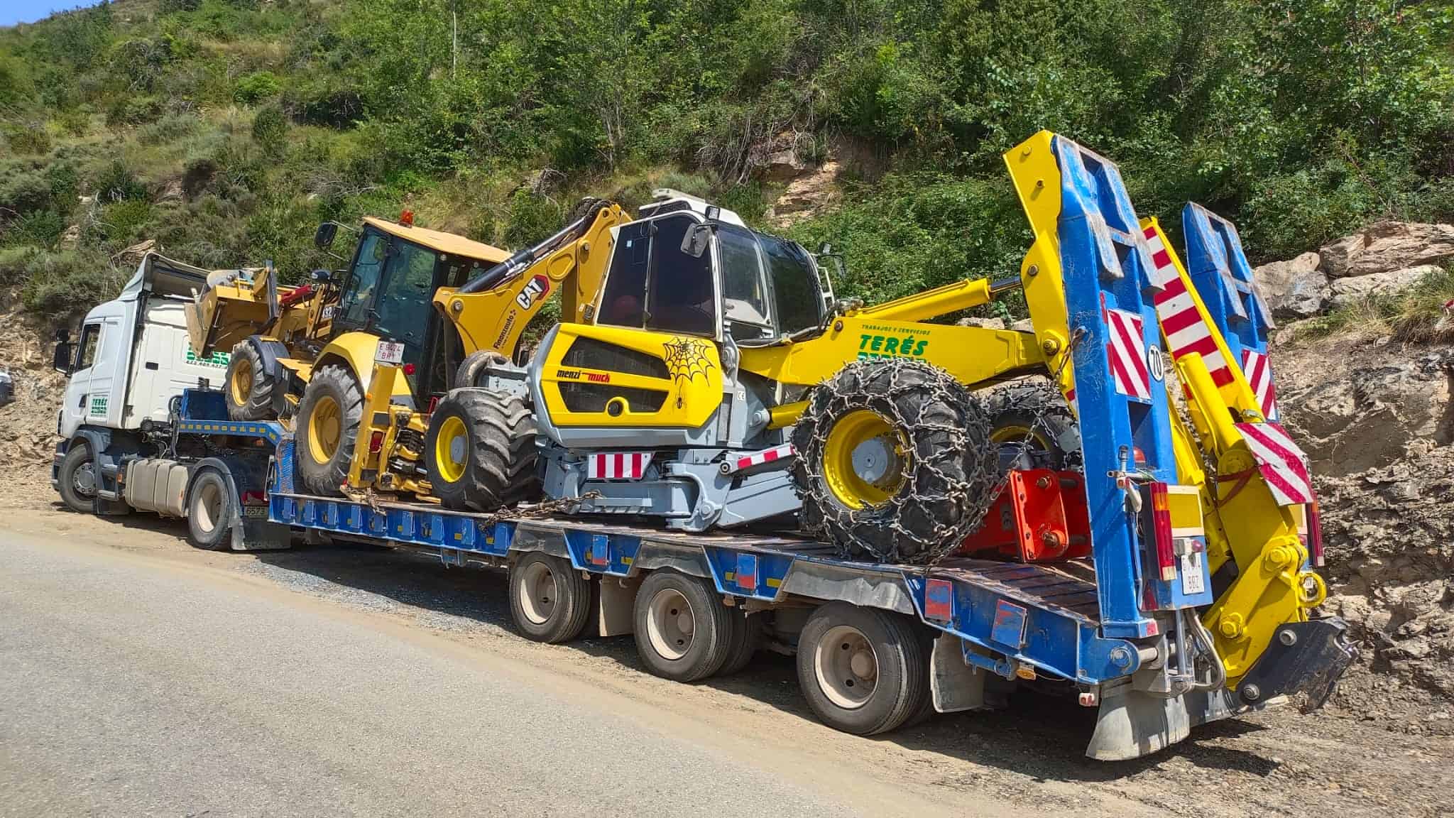 Remolque de maquinaria de construcción y obras públicas con excavadoras y retroexcavadoras en ruta de montaña en Segovia, servicios de transporte y traslado de maquinaria pesada por Terés.