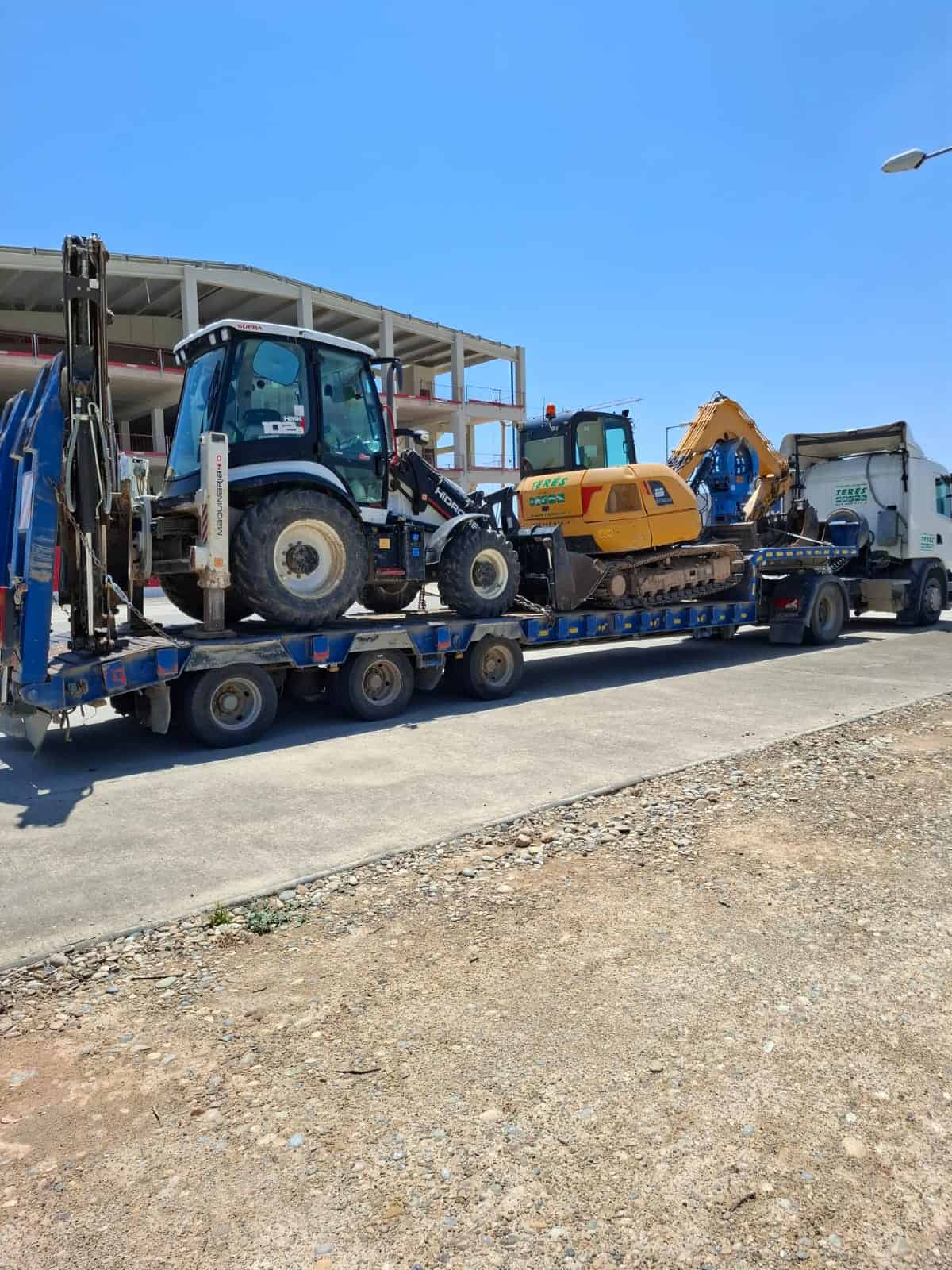 Transporte de maquinaria de obras públicas en trailer, incluyendo excavadoras y retroexcavadoras, para trabajos de construcción y reformas en obras de calidad.